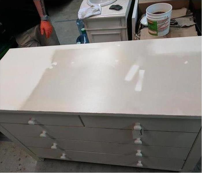 Pictured is a white bedroom dresser covered in soot that is ready for cleaning