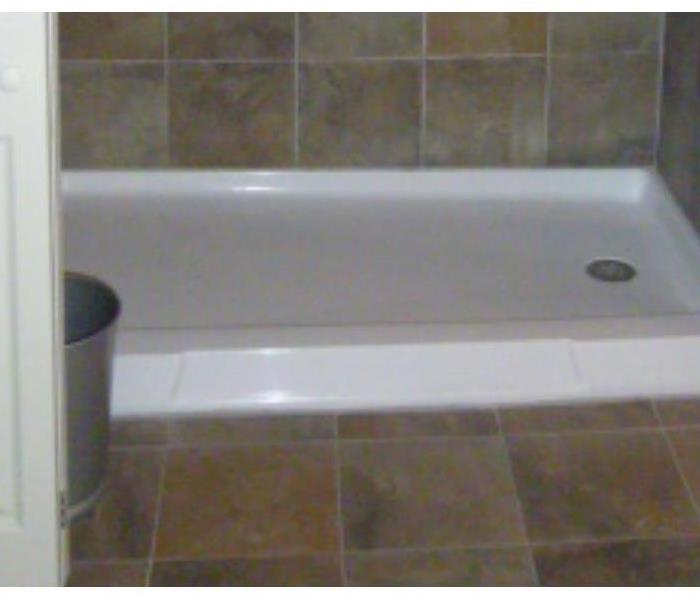 Photo taken from the same perspective after cleaning, showing a gleaming shower base and clean tile and grout