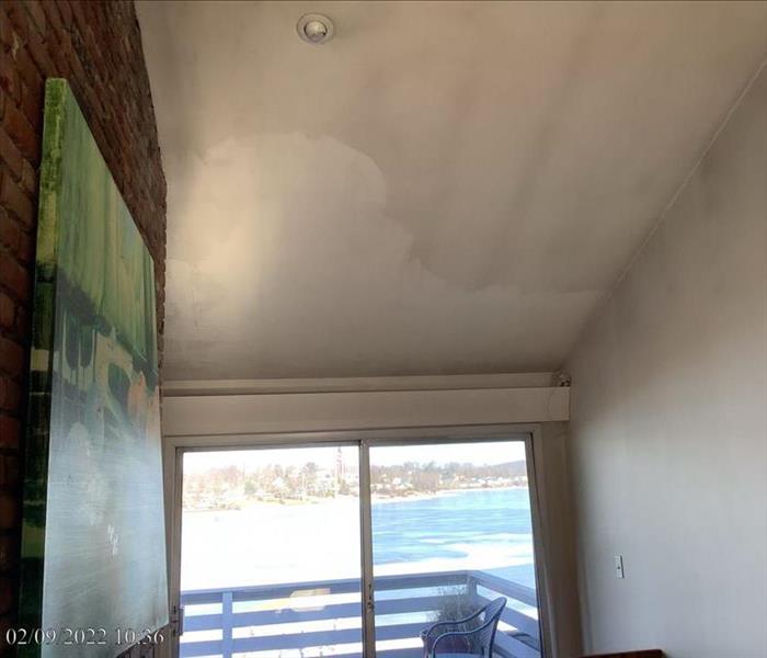 A moderately soot-stained ceiling and upper wall near a waterside patio