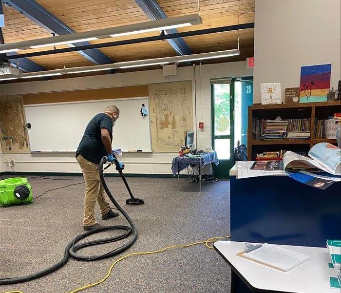 employee vacuuming water off carpet in school room